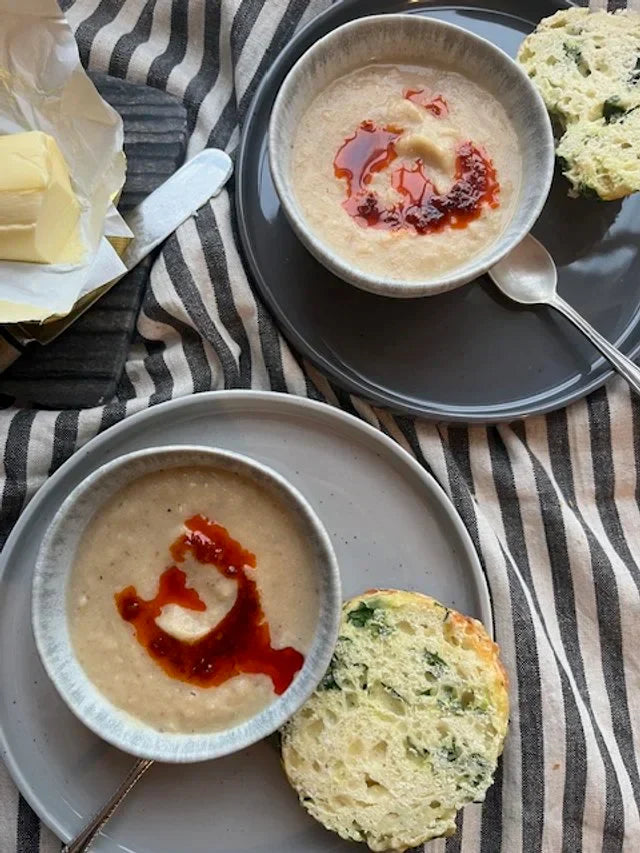 bowls of cauliflower soup, cheese scones, on stripe napkin with red chipotle oil