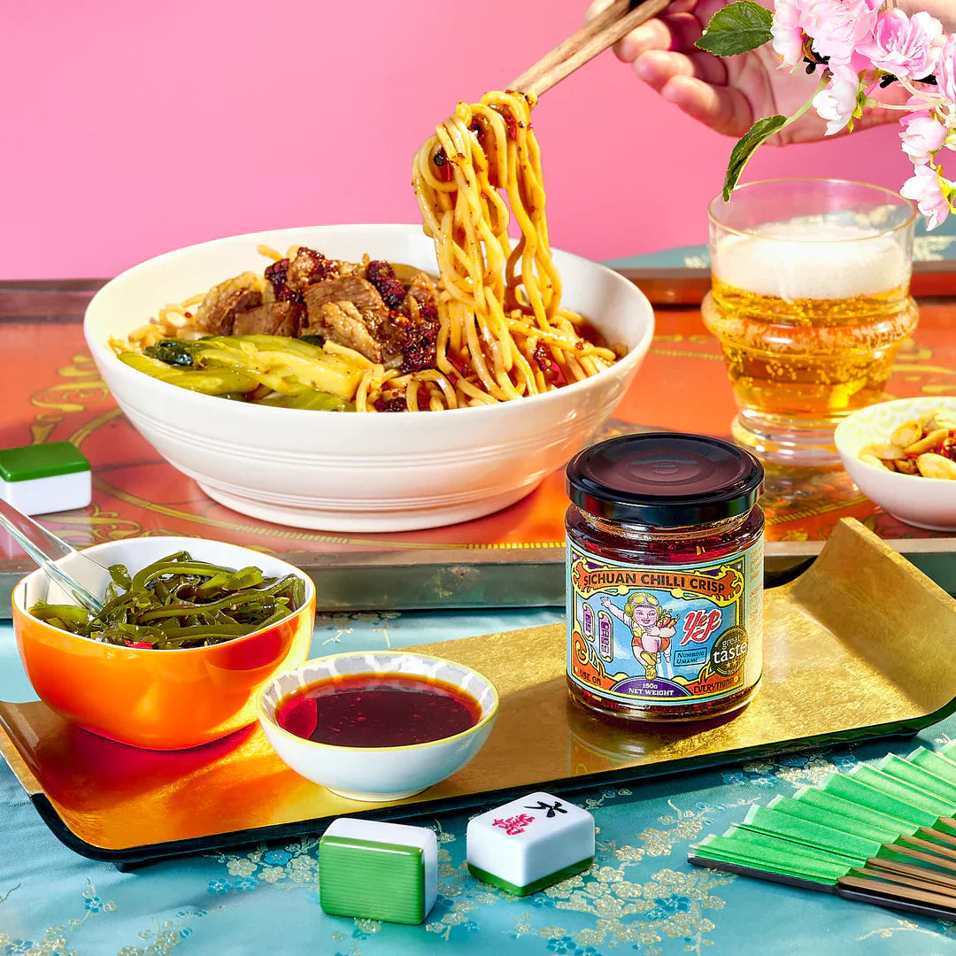 bowl of noodles with chilli oil, beer and a colourful backgroud