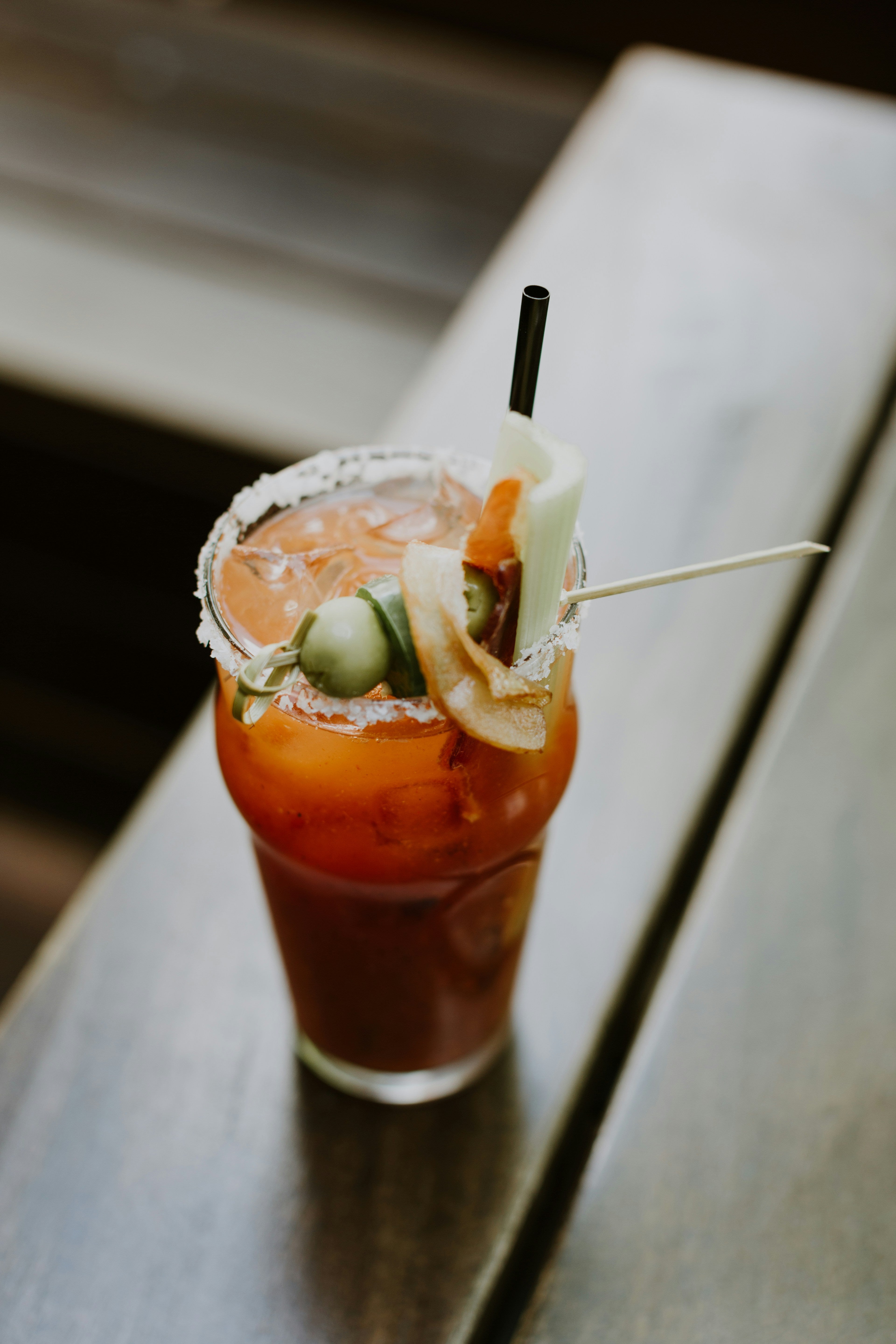 Spicy Bloody Mary cocktail served over ice with pickled garnish and chilli salt rim, photographed in natural light.