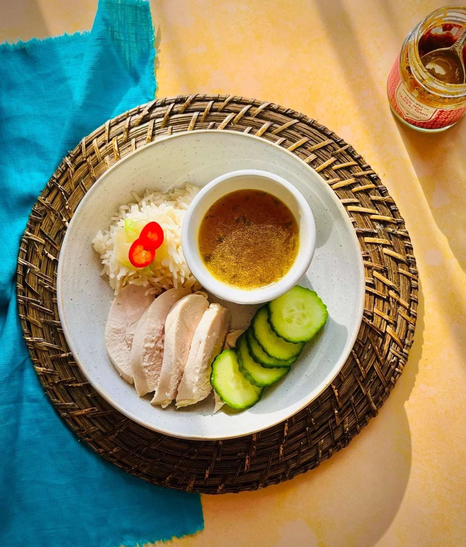 white bowl with chicken, broth, rice and chilli on a prange table and blue napkin