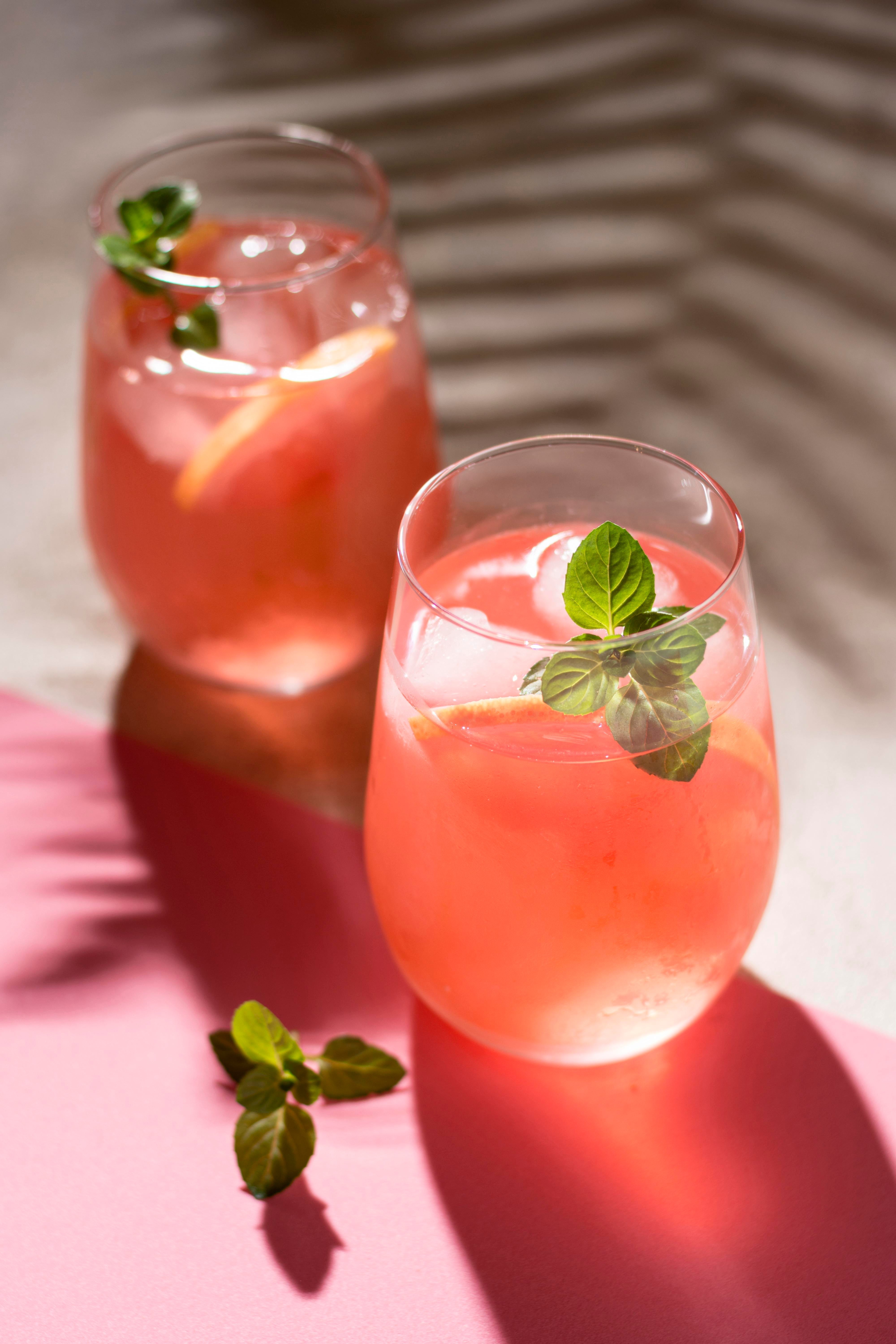 Refreshing pink grapefruit Paloma cocktails served over ice with fresh mint and citrus slices in soft sunlight.