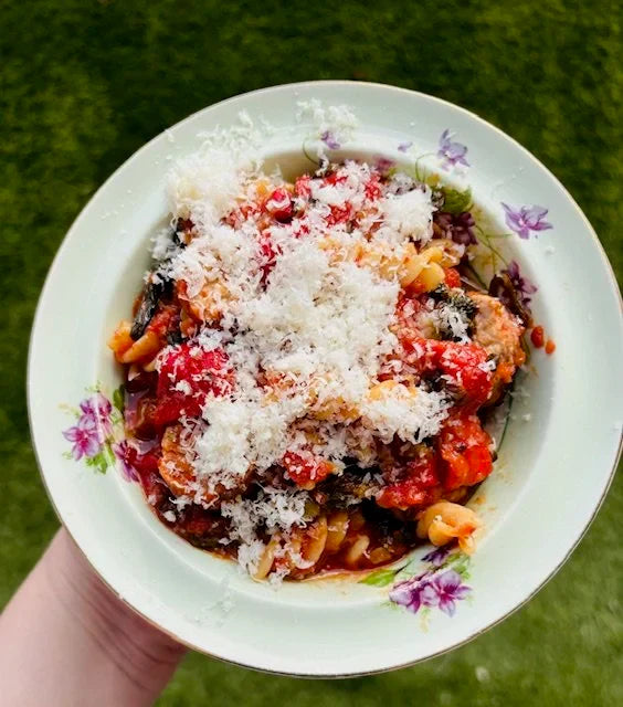 bowl of pasta with sausage, peppers, tomatoes covered in cheese