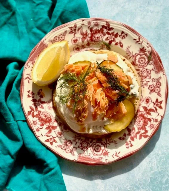 pink floral plate with blue napkin, crumpet with smoked trout, egg, dill, pickles, lemon