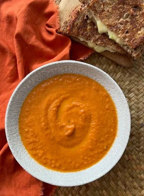 bowl of tomato soup with orange napkin and cheese and tomato toastie