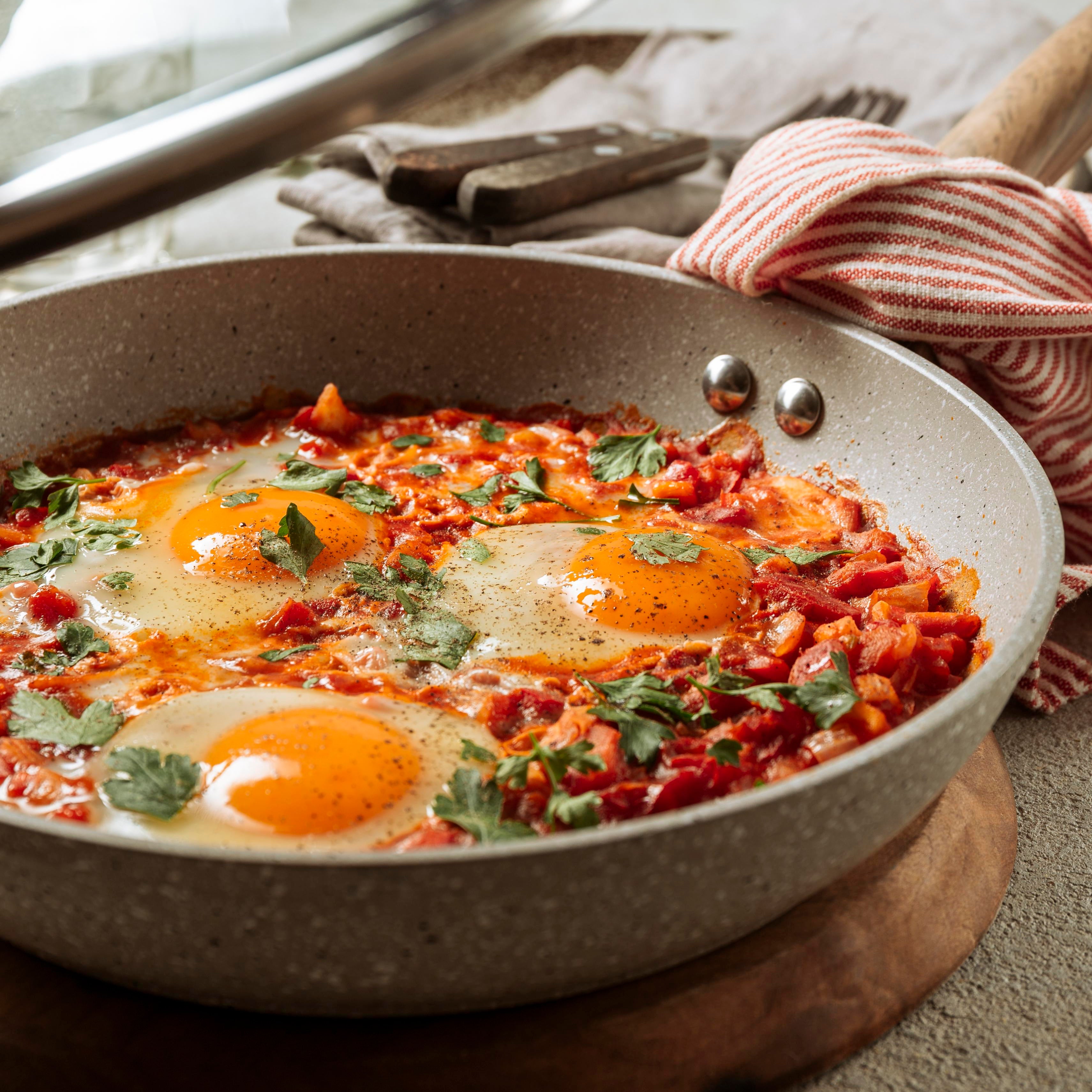 Frying pan with eggs and vegetables on a wooden surface