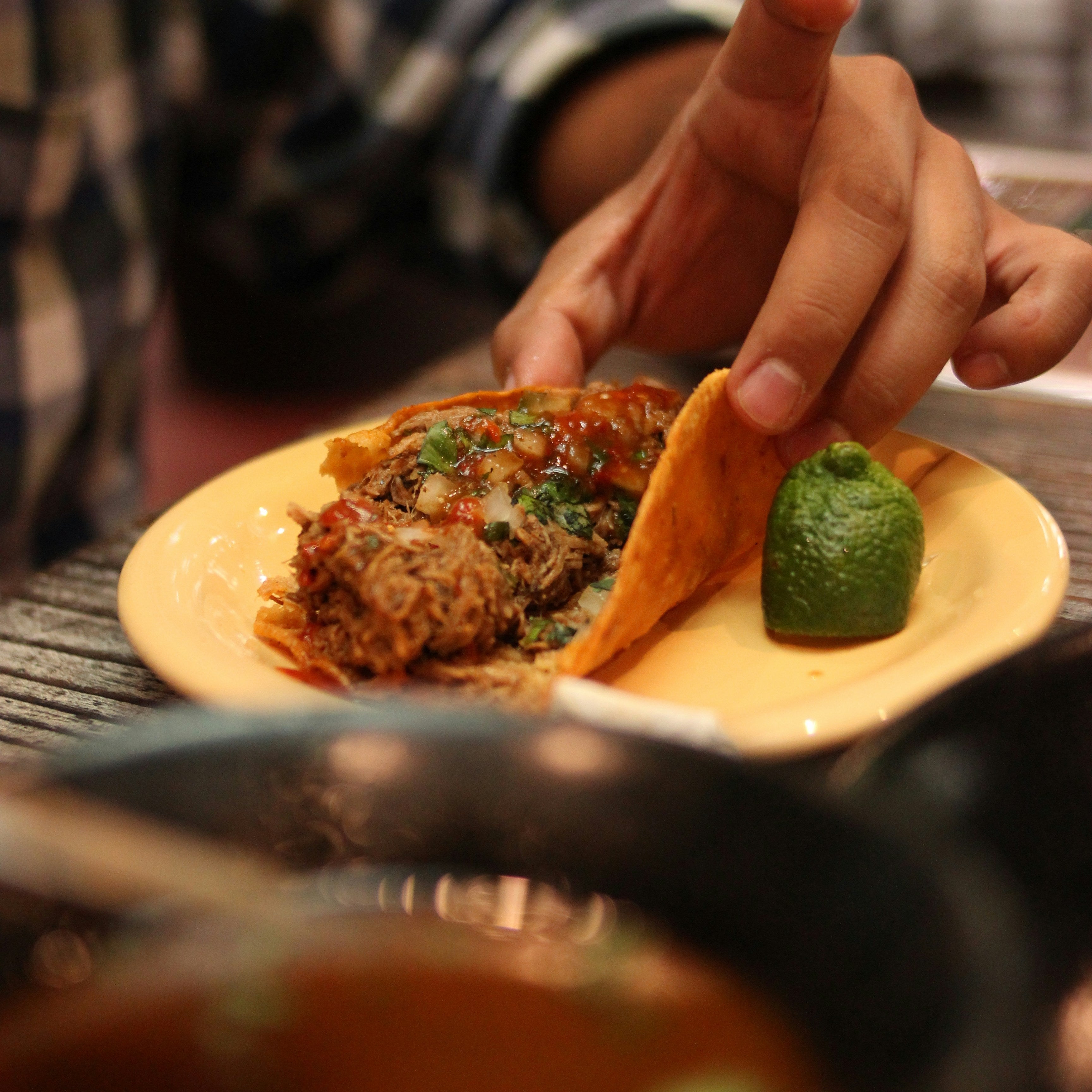 Person holding a taco with a side of salsa and lime on a plate.