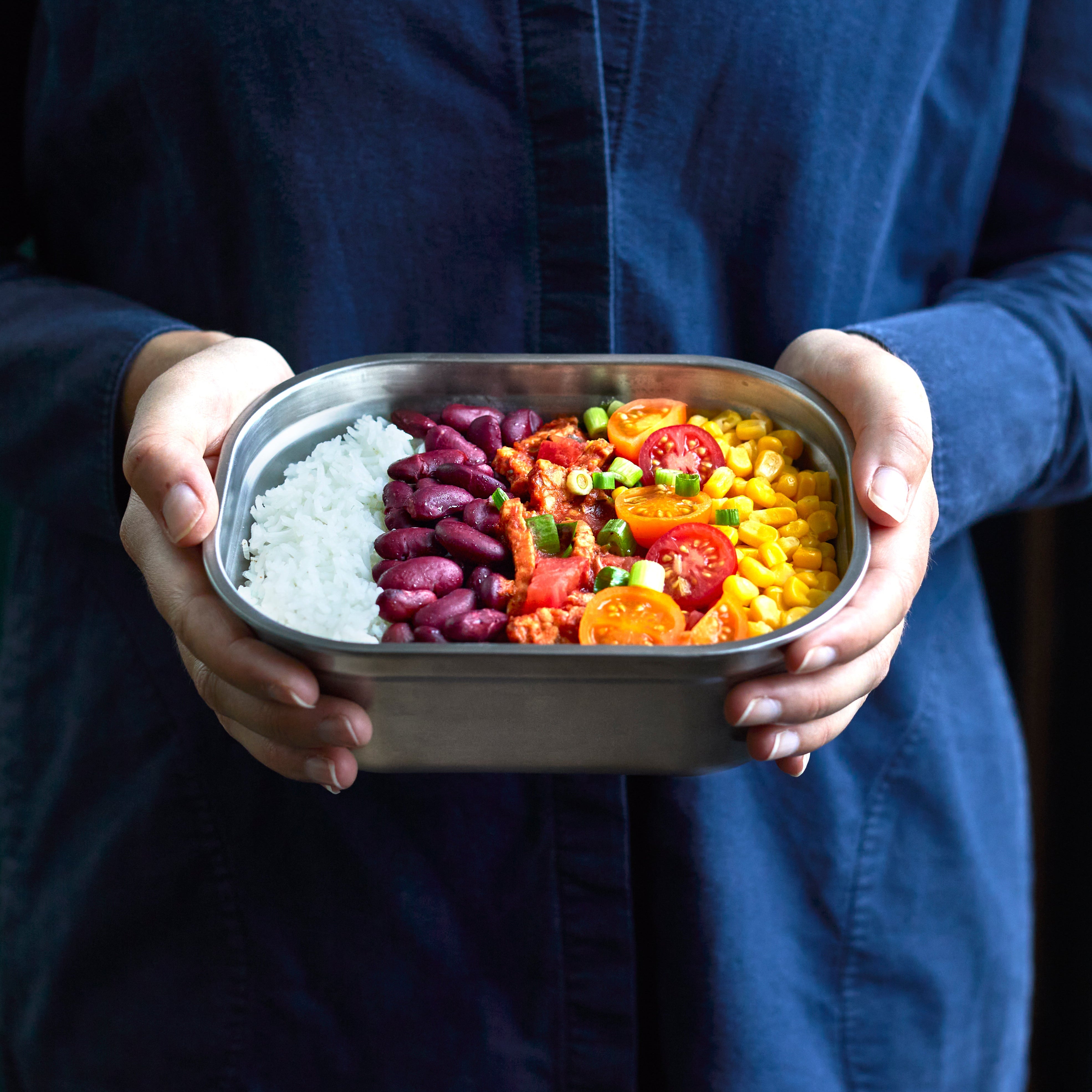 Person holding a metal lunch box with a colorful salad.