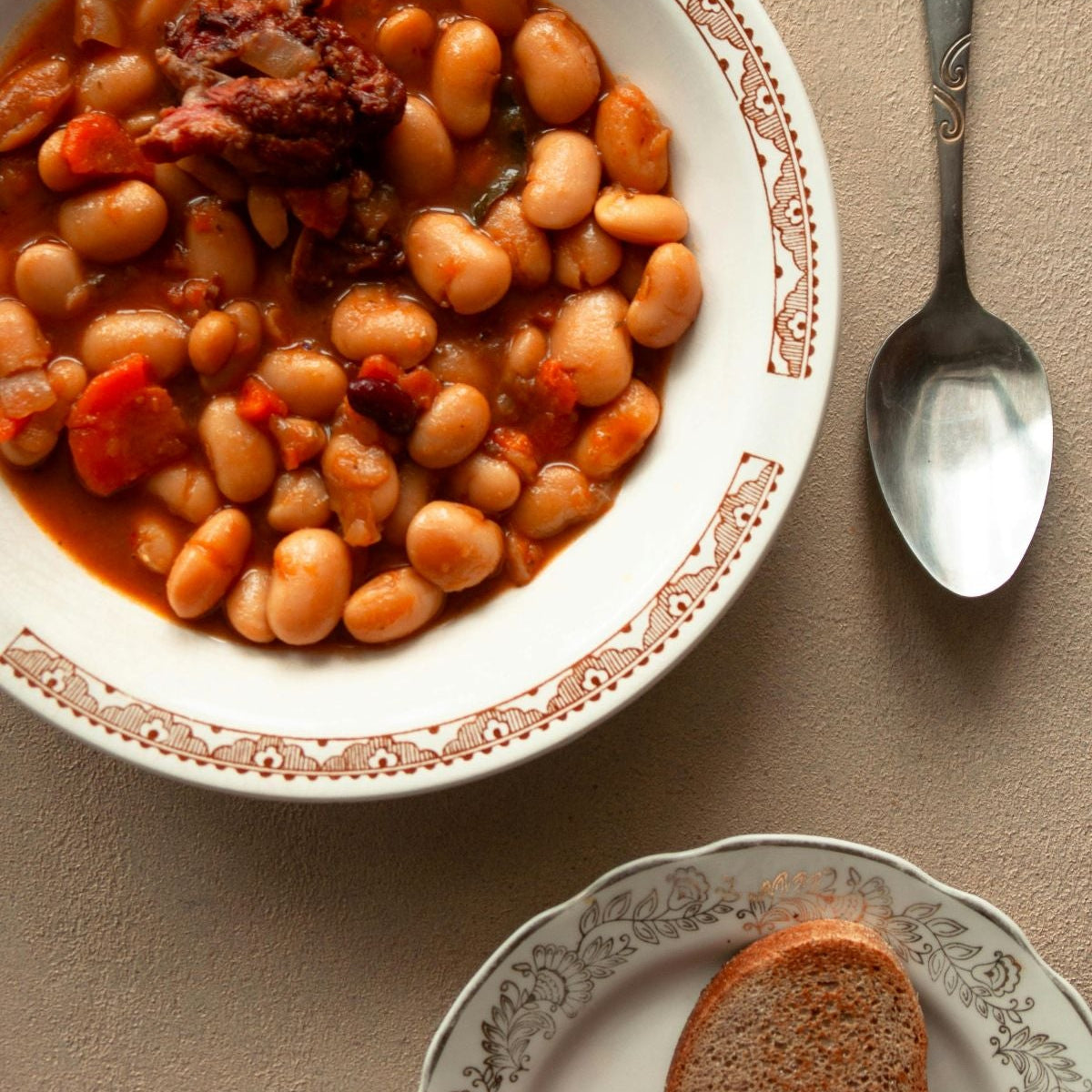 Bowl of bean stew with a side of bread on a beige surface