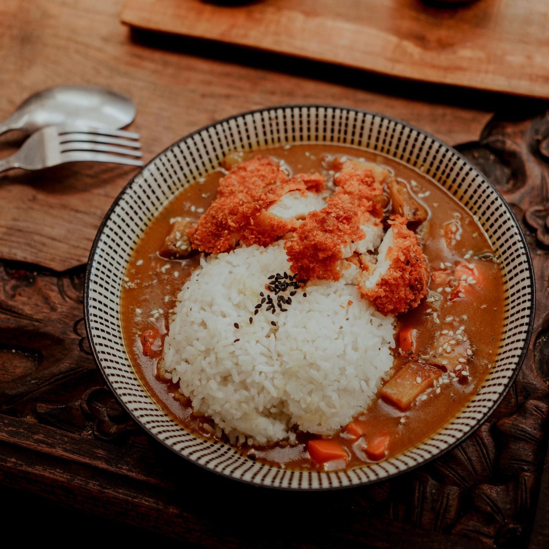 Curry dish with rice and fried chicken on a wooden table with a sake bottle and cup.