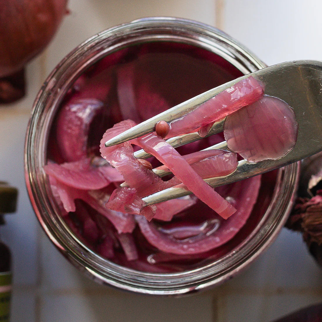 Pickled red onions in a jar with a fork holding some onions above.