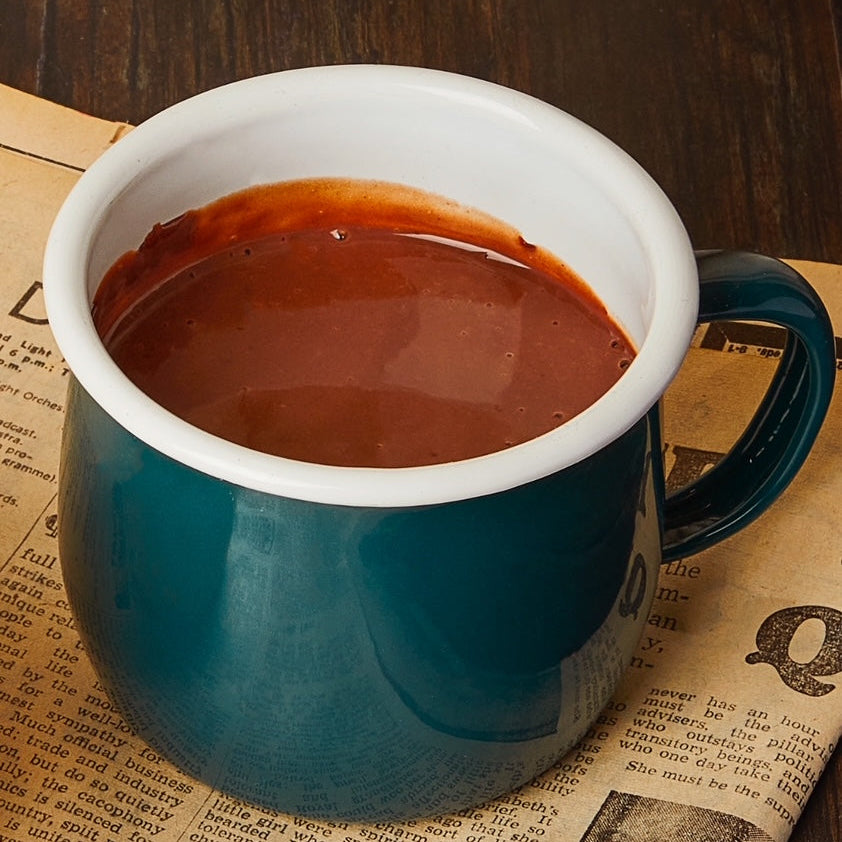 Blue mug with hot chocolate on a wooden surface with newspaper
