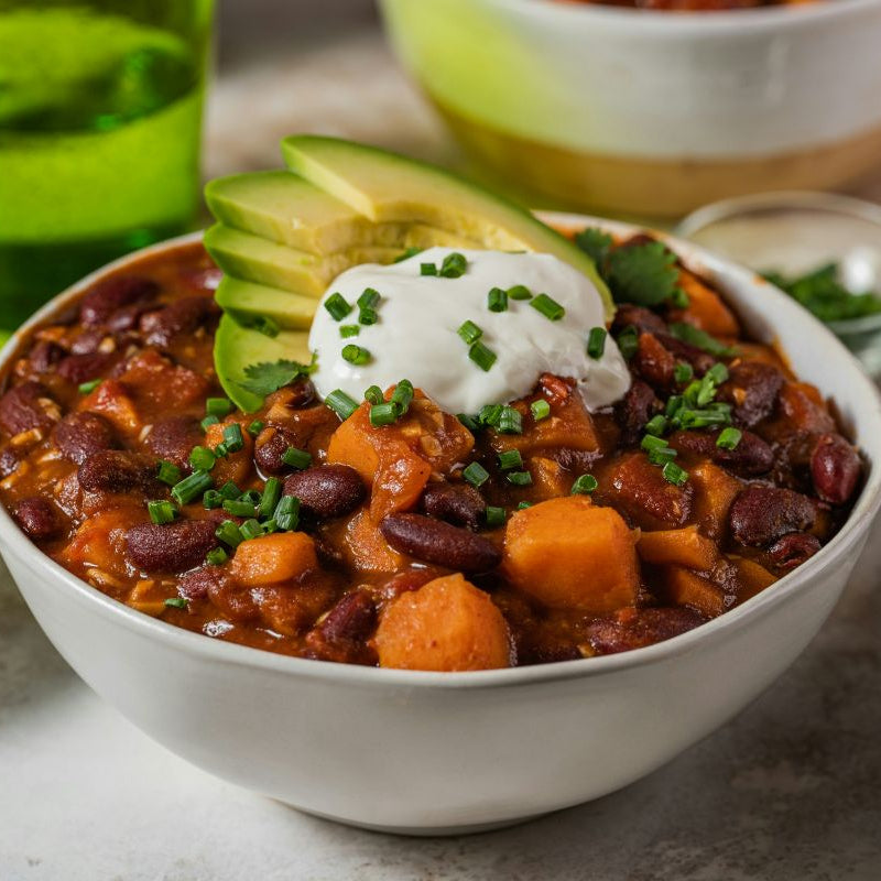 Bowl of chili with toppings on a table with drinks and garnishes.