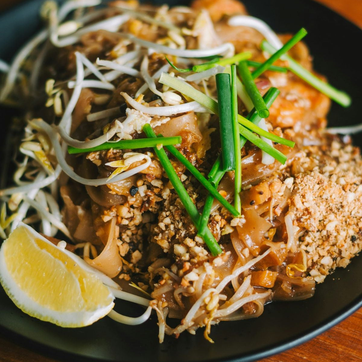 Plated dish of pad Thai with garnishes on a wooden table