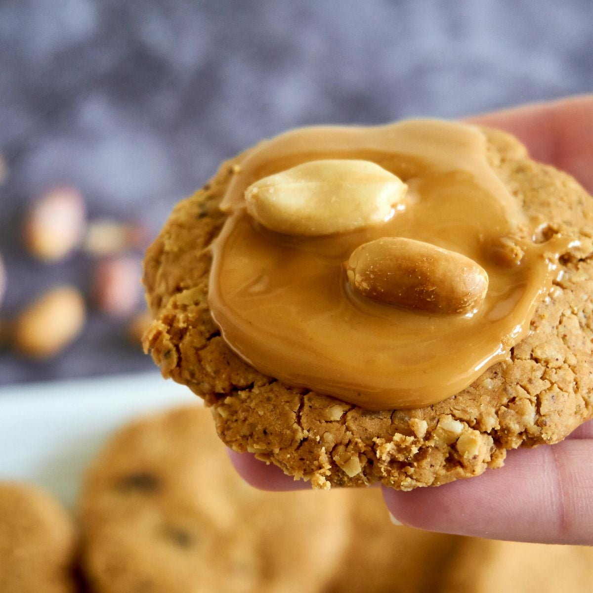 Cookie with peanut butter and almonds held by a hand, blurred cookies in the background