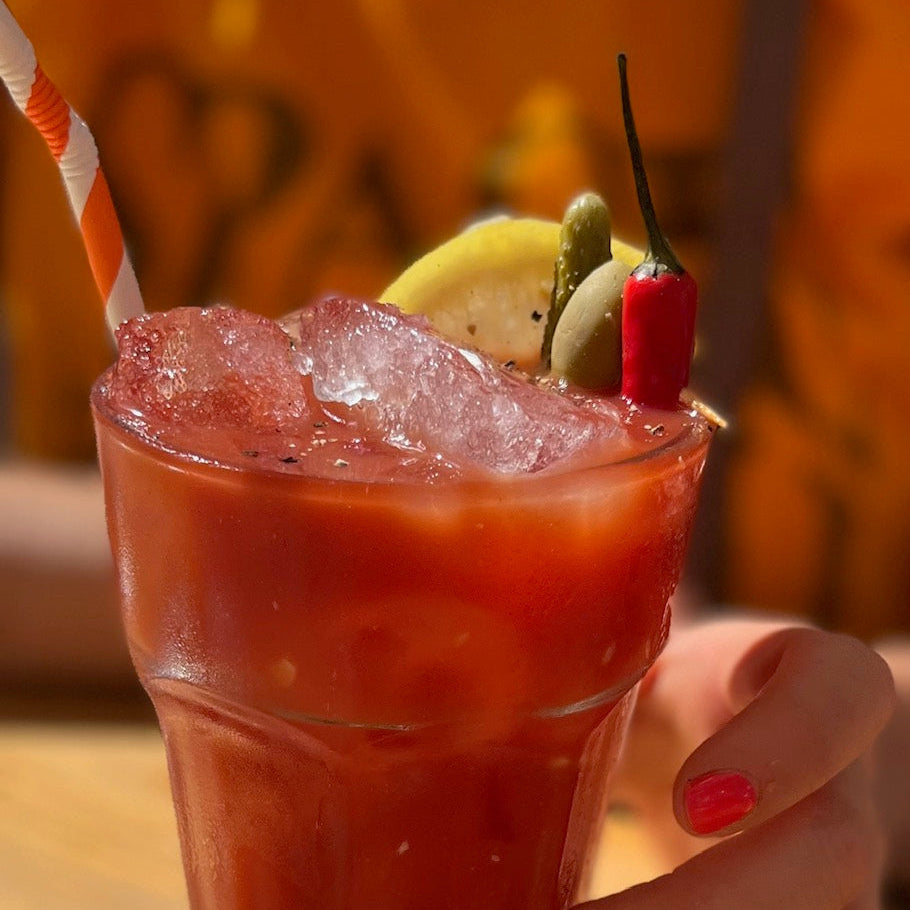 Bloody Mary cocktail with a garnish of peppers and a straw, held by a hand.
